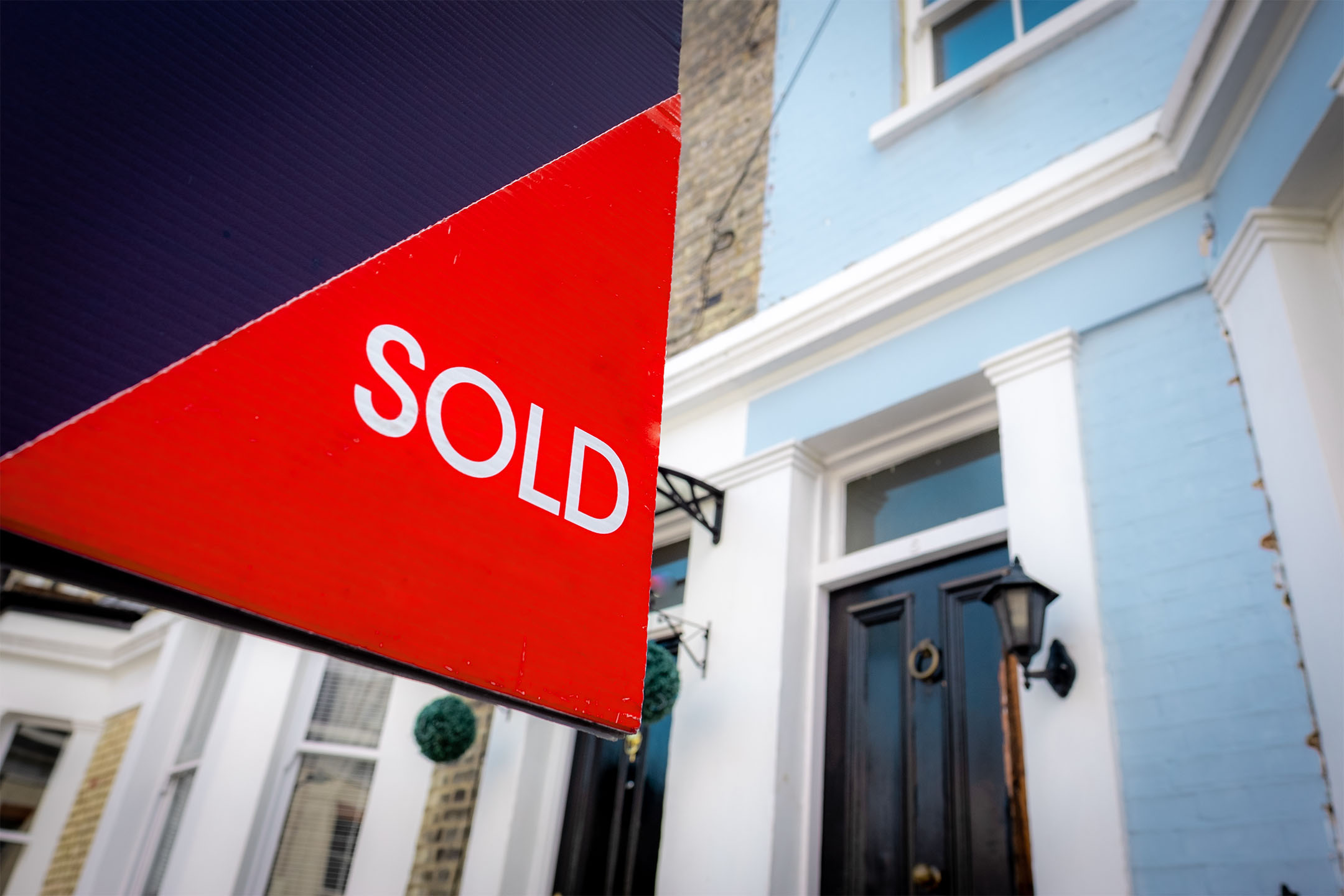 Estate agent SOLD sign with houses in background